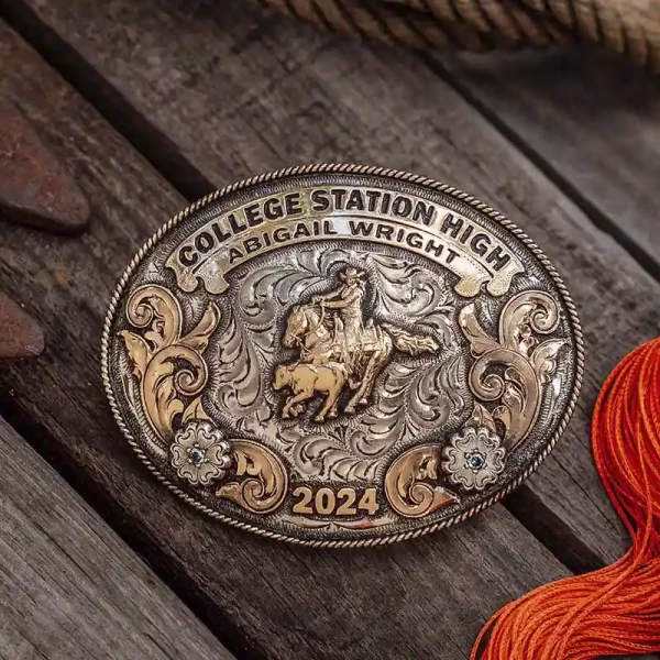 A custom rodeo belt buckle for College Station High with personalized name featuring a team roping rodeo figure, golden scrolls and flowers
